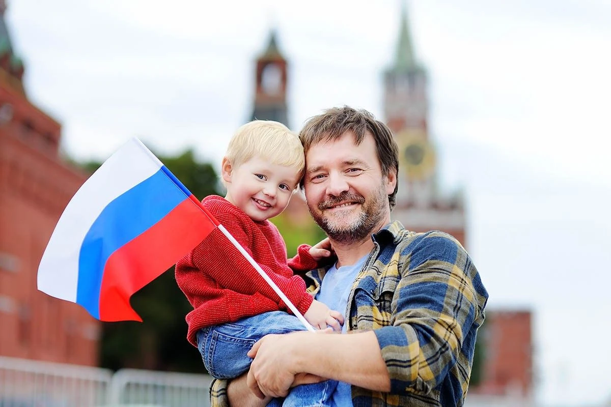 мужчина с маленьким ребенком на руках держит флаг России